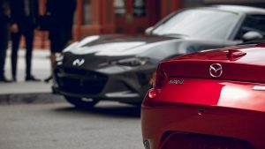 A pair of 2020 Mazda MX-5 Miata's passing on a city street.